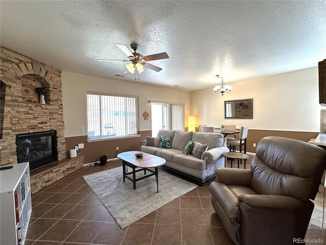 living room featuring a fireplace, a textured ceiling, ceiling fan with notable chandelier, and dark tile patterned flooring