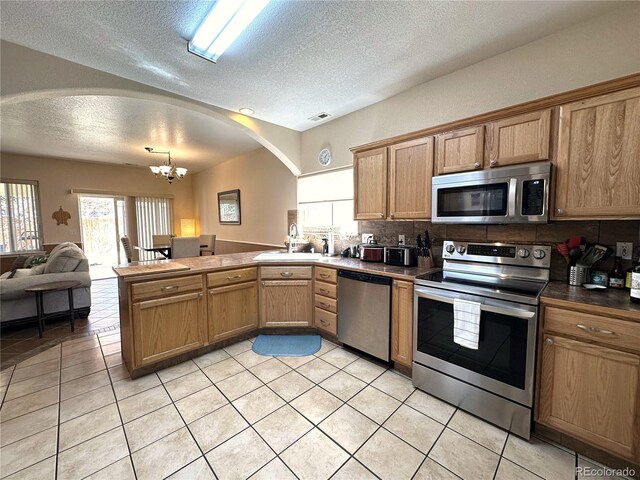 kitchen featuring an inviting chandelier, a sink, a peninsula, a textured ceiling, and stainless steel appliances