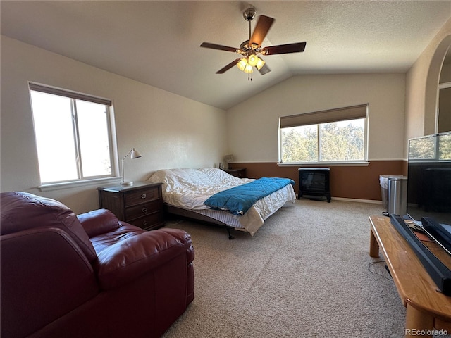carpeted bedroom with a ceiling fan, a wood stove, multiple windows, and lofted ceiling