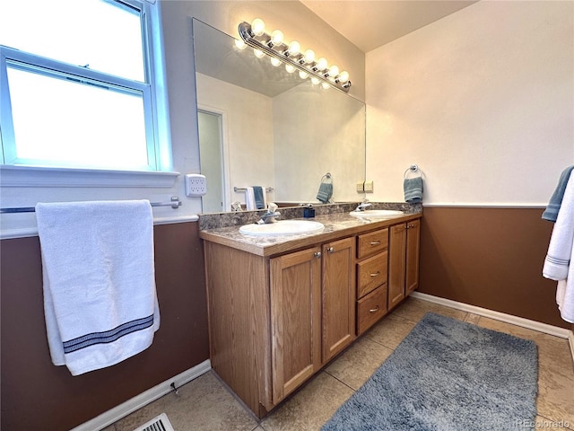 full bath featuring double vanity, a sink, tile patterned flooring, and baseboards