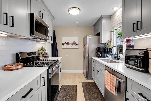 kitchen featuring gray cabinetry, sink, light hardwood / wood-style flooring, and stainless steel appliances