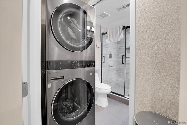 laundry room with tile patterned flooring, a textured ceiling, and stacked washer / dryer