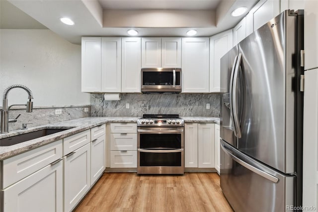 kitchen with stainless steel appliances, light stone countertops, sink, and white cabinets