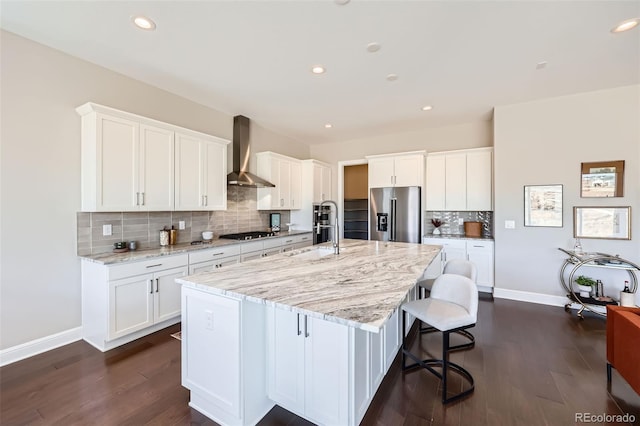 kitchen with black gas cooktop, high end refrigerator, wall chimney range hood, a large island, and white cabinets