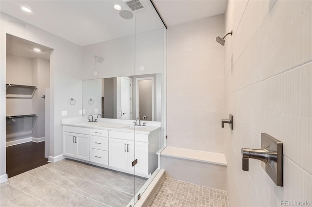 bathroom featuring vanity, tile patterned floors, tile walls, and a tile shower