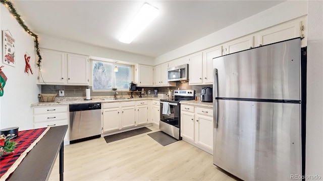 kitchen featuring white cabinetry, stainless steel appliances, tasteful backsplash, light stone counters, and light wood-type flooring