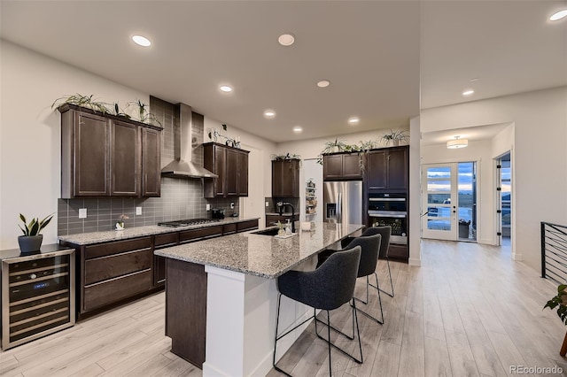 8868 Geyser Peak Way, Parker, CO 80138 - kitchen featuring wine cooler, wall chimney range hood, a sink, appliances with stainless steel finishes, and light wood-type flooring
