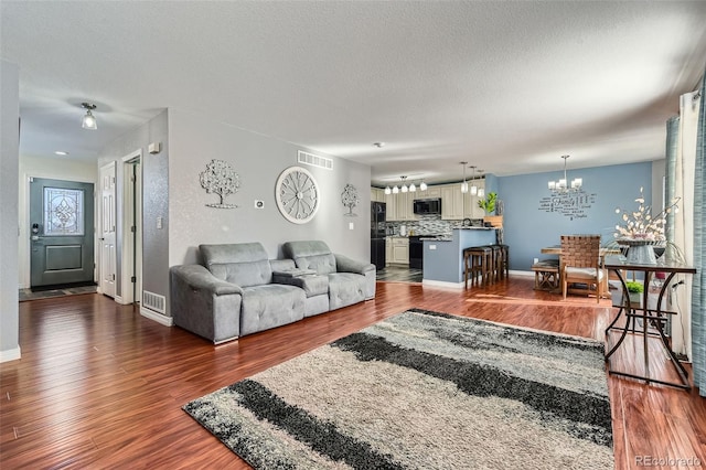 living room featuring an inviting chandelier, dark hardwood / wood-style floors, and a textured ceiling