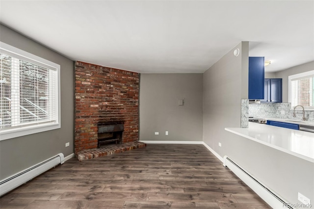 unfurnished living room featuring a brick fireplace, dark wood-type flooring, and a baseboard heating unit