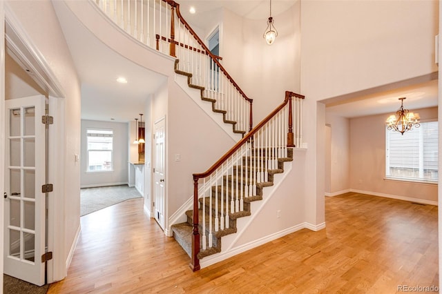 staircase with baseboards, wood finished floors, a towering ceiling, and an inviting chandelier