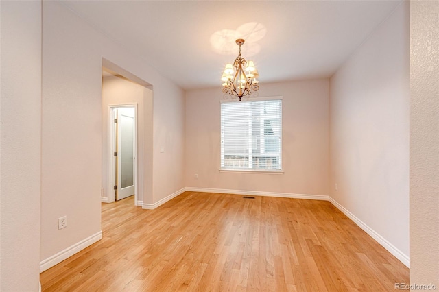 empty room featuring baseboards, a notable chandelier, visible vents, and light wood-type flooring