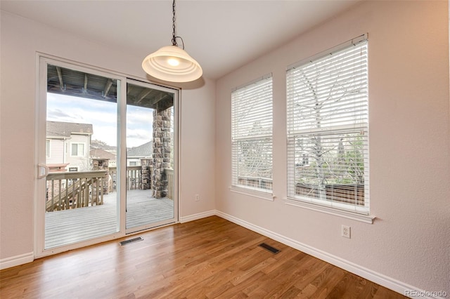 unfurnished dining area with wood finished floors, plenty of natural light, baseboards, and visible vents