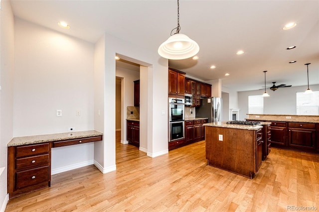 kitchen featuring light wood-type flooring, built in study area, appliances with stainless steel finishes, and pendant lighting