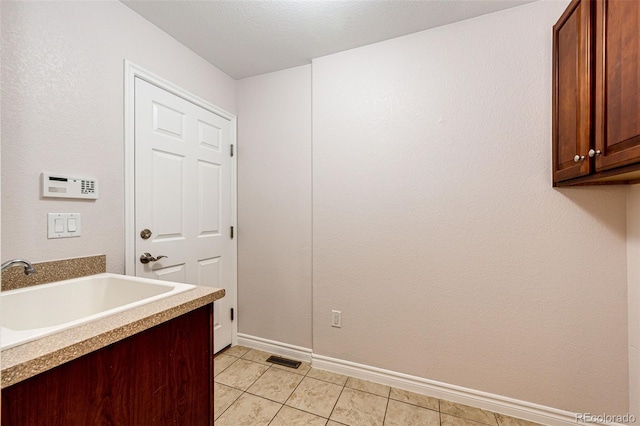 clothes washing area with a sink, visible vents, baseboards, cabinet space, and light tile patterned floors