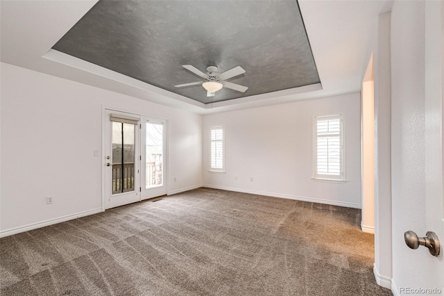 carpeted empty room featuring ceiling fan, baseboards, visible vents, and a raised ceiling