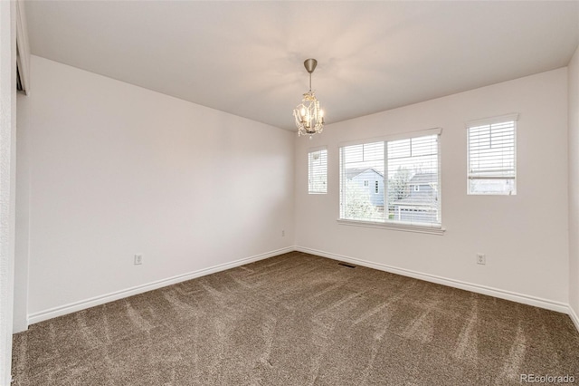 spare room with a chandelier, dark carpet, visible vents, and baseboards