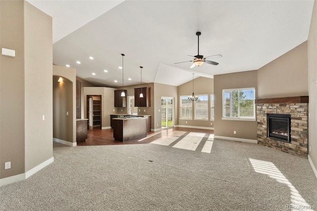 unfurnished living room with ceiling fan with notable chandelier, a fireplace, vaulted ceiling, and dark carpet