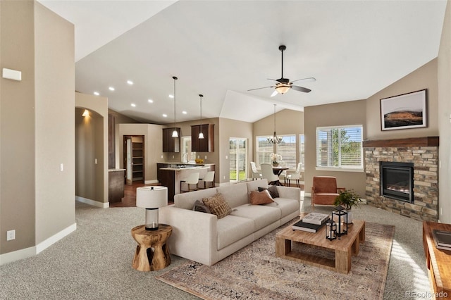 carpeted living room with a stone fireplace, ceiling fan with notable chandelier, and lofted ceiling