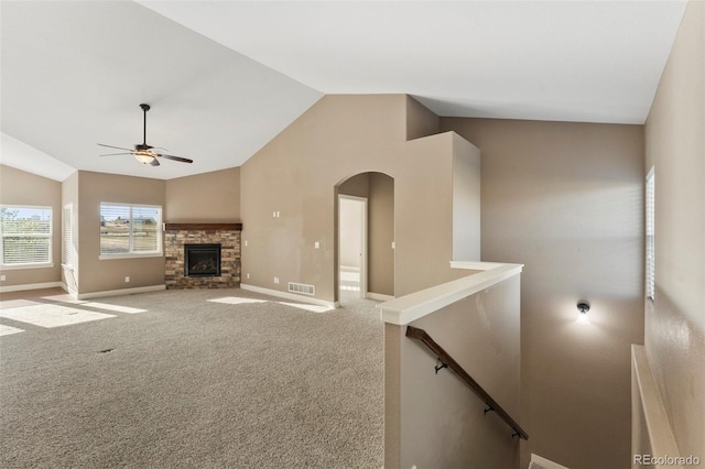 unfurnished living room featuring a stone fireplace, carpet flooring, vaulted ceiling, and ceiling fan