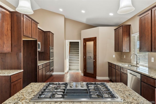 kitchen with light stone counters, hanging light fixtures, sink, appliances with stainless steel finishes, and vaulted ceiling