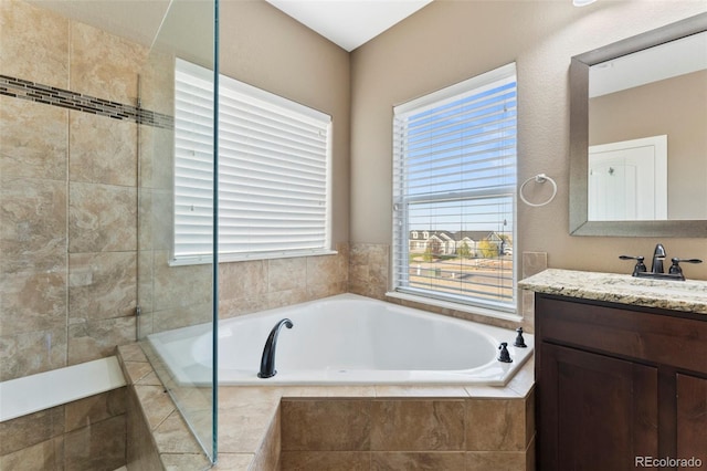 bathroom featuring a wealth of natural light, tiled bath, and vanity