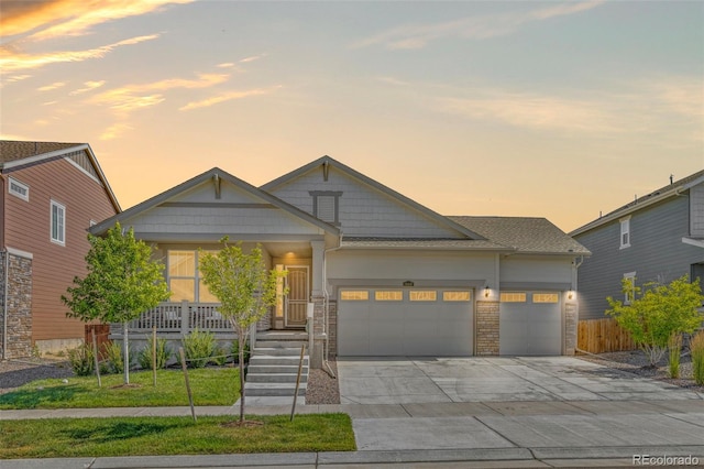 craftsman house with a porch, driveway, fence, an attached garage, and stone siding