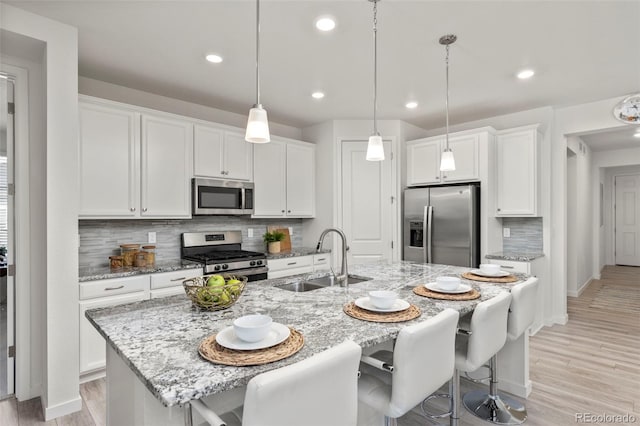 kitchen featuring a kitchen island with sink, white cabinets, tasteful backsplash, a sink, and stainless steel appliances