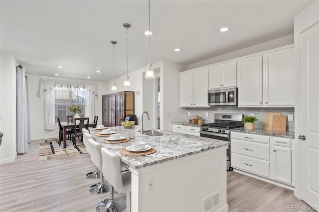 kitchen with a breakfast bar, white cabinetry, light wood-style flooring, backsplash, and stainless steel appliances