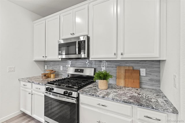 kitchen featuring appliances with stainless steel finishes, backsplash, white cabinets, and light stone countertops