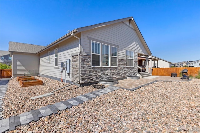 view of front of property featuring a patio, a fenced backyard, stone siding, and a vegetable garden