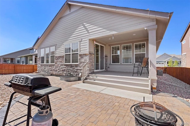 back of property with stone siding, a fenced backyard, a patio area, a porch, and an outdoor fire pit
