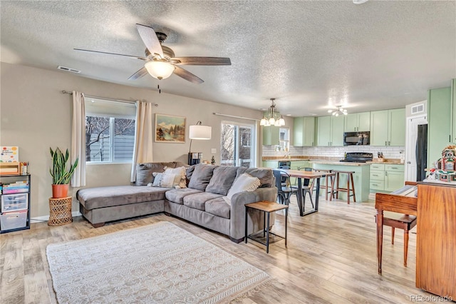 living room featuring ceiling fan with notable chandelier, light hardwood / wood-style floors, and a textured ceiling