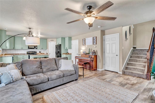 living room featuring ceiling fan, sink, light wood-type flooring, and a textured ceiling