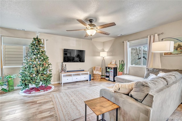 living room featuring ceiling fan, light hardwood / wood-style flooring, and a textured ceiling