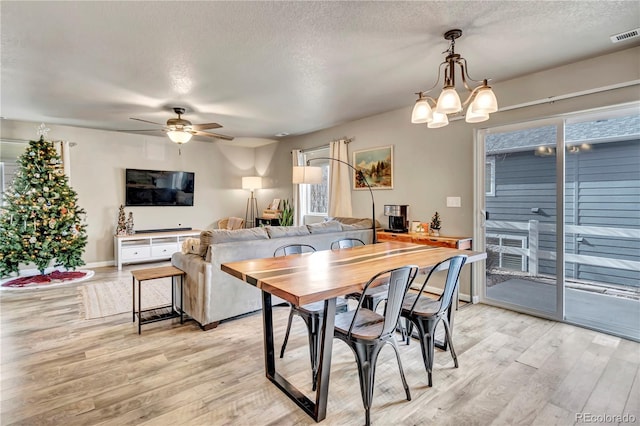 dining space featuring a textured ceiling, light hardwood / wood-style flooring, and ceiling fan with notable chandelier