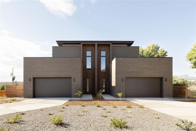 contemporary house featuring brick siding, an attached garage, concrete driveway, and fence