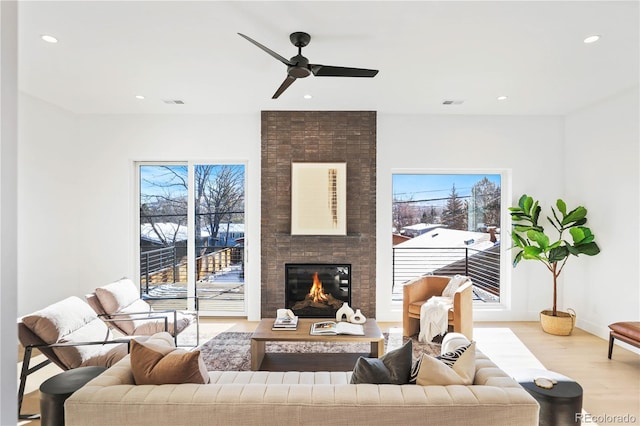 living area featuring recessed lighting, visible vents, a brick fireplace, and light wood finished floors