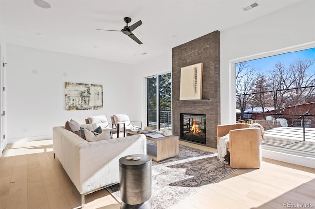 living room with a brick fireplace, wood finished floors, visible vents, and ceiling fan