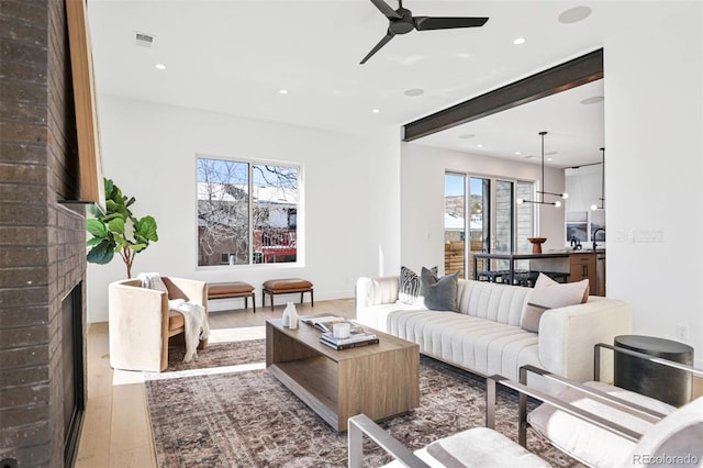 living room featuring visible vents, a brick fireplace, a healthy amount of sunlight, and wood finished floors