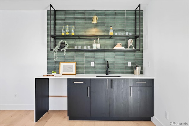 bar with a sink, light wood-type flooring, baseboards, and tasteful backsplash