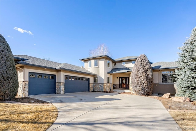 prairie-style home with an attached garage, stone siding, concrete driveway, and stucco siding