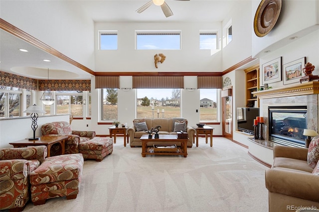 living area with baseboards, light carpet, a fireplace, ceiling fan, and built in shelves