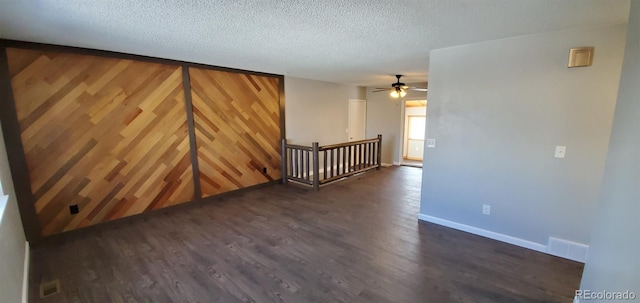 spare room with wooden walls, baseboards, visible vents, dark wood finished floors, and a textured ceiling