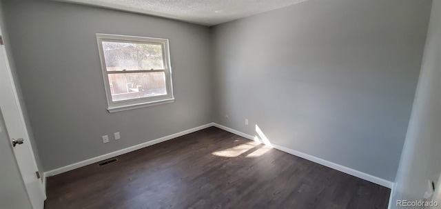 empty room featuring visible vents, dark wood finished floors, a textured ceiling, and baseboards