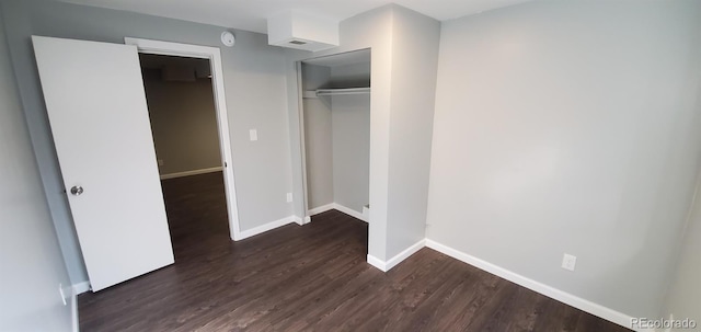 unfurnished bedroom with dark wood-style floors, baseboards, and a closet