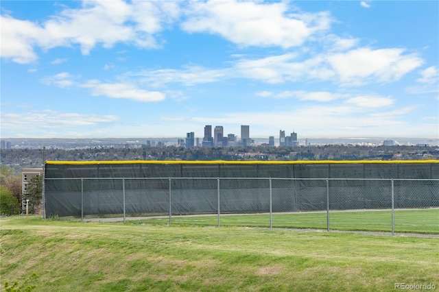 view of tennis court featuring fence, a city view, and a yard
