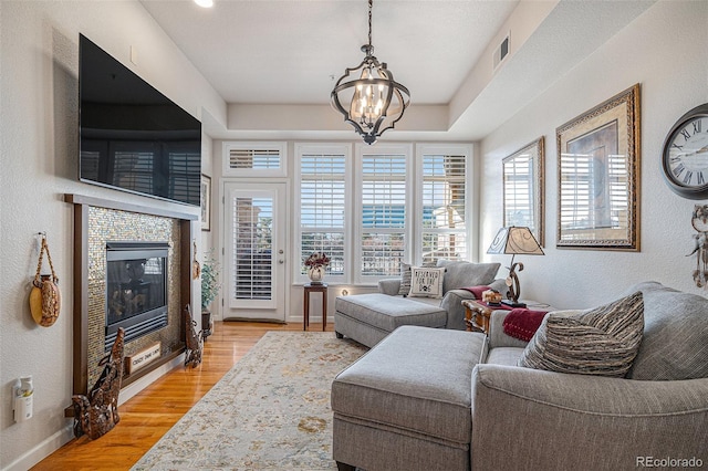 living room with light wood-type flooring, a notable chandelier, and a tile fireplace