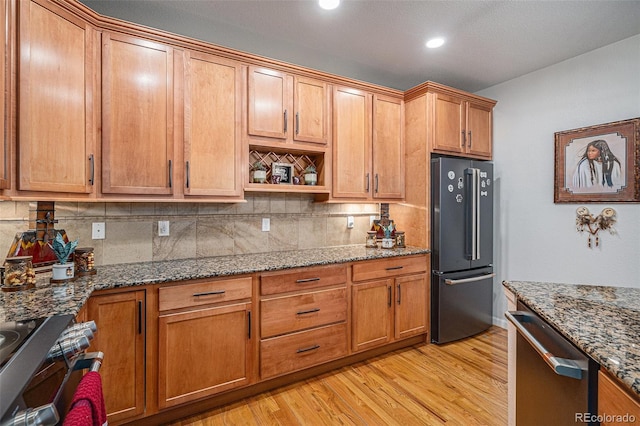 kitchen with backsplash, appliances with stainless steel finishes, stone counters, and light hardwood / wood-style floors