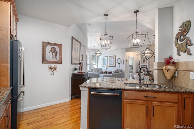 kitchen with black dishwasher, decorative light fixtures, dark stone counters, stainless steel refrigerator, and sink