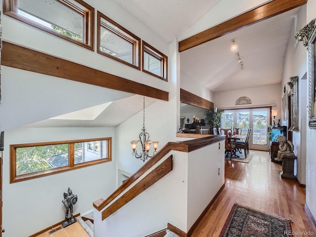 hall featuring an inviting chandelier, rail lighting, light hardwood / wood-style flooring, vaulted ceiling, and a textured ceiling